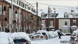 A man shovels snow from around his car on a street in Goole