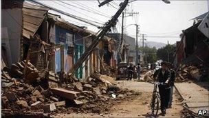 Man pushes his bicycle past ruined buildings in Talca Chile