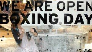 An employee applies a sign informing shoppers that they will be open on Boxing Day