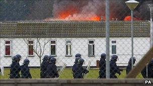 Specialist prison officers in riot gear in front of one of Ford's burning buildings