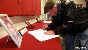 A man signs condolence books for Antoine de Leocour and Vincent Delory (10 Jan 2011)