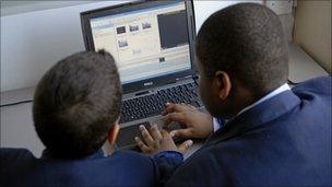 Two boys type on a laptop computer