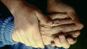 Elderly person and helper hold hands