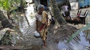 A woman carries a pot of drinking water at her flooded house in Kartivu, east of Colombo