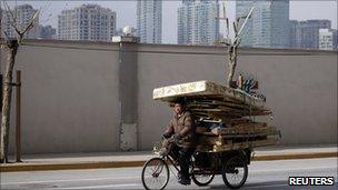 A man rides a tricycle cart past high-rises in Shanghai on 10 Jan 2011