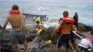 People clamber on the rocky shore on Christmas Island during a rescue attempt as a boat breaks up in the background