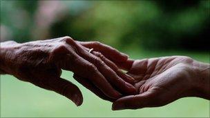 An elderly lady's hand reaching out to a young person's hand.