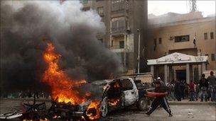 A protester throws a traffic cone into a burning car, in Giza, Egypt