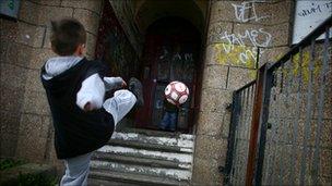 Boy playing football next to run down houses