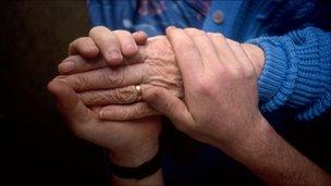 Carer holds elderly patient's hand