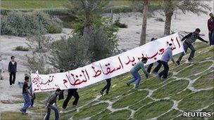 Protesters carry a banner as they walk at the Pearl Roundabout in the Bahraini capital Manama, 15 February 2011