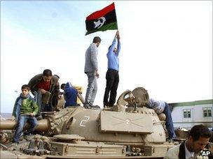 A man holds a pre-Gaddafi Libyan flag on top of a tank in Benghazi (21 February 2011)