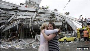 Two women hug each other in front of a collapsed building in central Christchurch