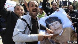 Protesters deface a poster of Col Gaddafi