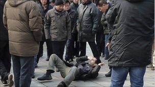 A journalist lies on the ground surrounded by the men who pushed him, in Beijing on 27 February 2011