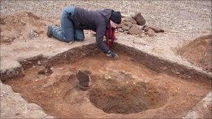 Archaeologists excavate the ground around the stone