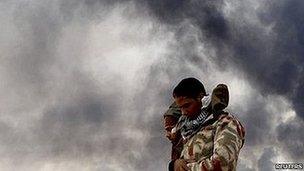 Rebel fighters pray in front of a burning gas storage terminal during a battle on the road between Ras Lanuf and Bin Jawad, 9 March 2011