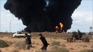 Rebels walk past a burning oil terminal hit by pro-Gaddafi forces near Ras Lanuf, 9 March