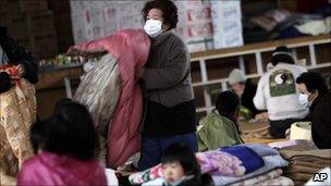 An evacuee makes a bed on the floor of a school gymnasium