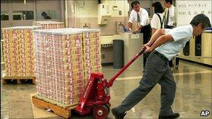 Bank of Japan employee pulls a cart carrying a stack of new yen banknotes