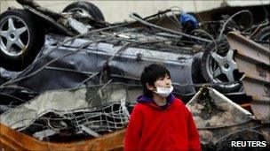 A boy looks on in front of an overturned car among debris in Otsuchi, Iwate prefecture