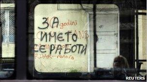 A woman sits in a bus as it passes a graffiti that reads "It's all about the name" in Skopje March 21, 2011