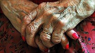 An elderly lady holds her hands on her lap