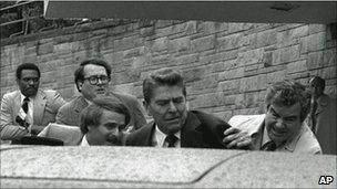 President Reagan is pushed into his waiting limousine by Secret Service agents after being shot