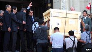 Peruvian President Alan Garcia waves to the press as workers carry a crate of Inca artefacts into a government office in Lima