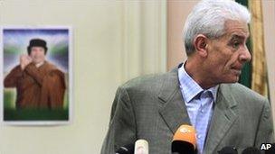 Libyan Foreign Minister Moussa Koussa speaking in Tripoli with a portrait of Muammar Gaddafi in the background, 18 March