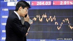 A businessman uses his mobile phone before a share prices board