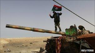 A rebel fighter walks on a tank along the road between Ajdabiya and Brega, 6 April