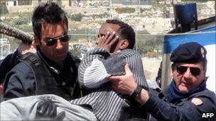 A migrant is carried by policemen to help him disembarking from a boat that capsized off Lampedusa, April 6, 2011