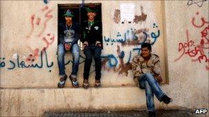 Libyan rebels sit on a wall covered in graffiti mocking Libya's leader Muammar Gaddafi, in the rebel-held city of Benghazi, eastern Libya on 14 April 2011