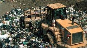 A tractor grinds over rubbish at a landfill