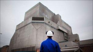 A workman in a hard hat looks up towards one of the buildings at Hinkley Point power station.