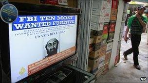 An Afghan youth walks past a television announcing the death of Osama Bin Laden