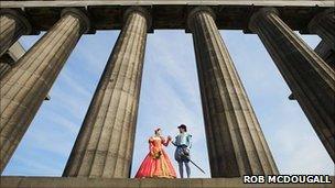 A man and a woman dressed in Tudor clothes stand together between columns