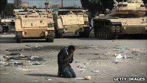 A protester prays near Egyptian army vehicles in Cairo. Photo: February 2011