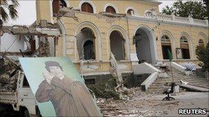 A poster of Libyan leader Gaddafi is seen in front of a government building damaged by coalition air strikes, according to the government, in Tripoli