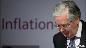 Mervyn King looking down facing a sign saying inflation