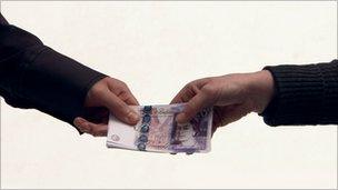 A bundle of £20 notes being passed from one hand to another.