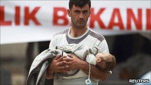 A man carrying a baby at a refugee camp in Yayladagi, Hatay province, Turkey, 14 June