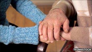 The hands of an elderly person being held by a younger person