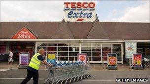 Tesco employee pushes trolleys in front of a branch