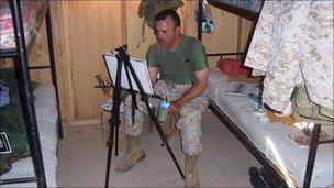 Michael Fay sitting in a military bunk, working on a painting