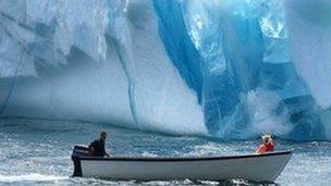 Two people in a boat moving past an iceberg