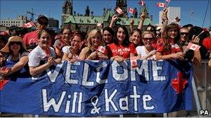 Well-wishers stand in front of a Welcome Wills and Kate banner