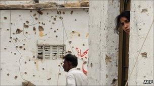 A woman peers from a doorway near a bullet-riddled wall in violence-hit Karachi, Pakistan, 9 July 2011