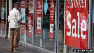 Man looking in shop window plastered with summer sales posters